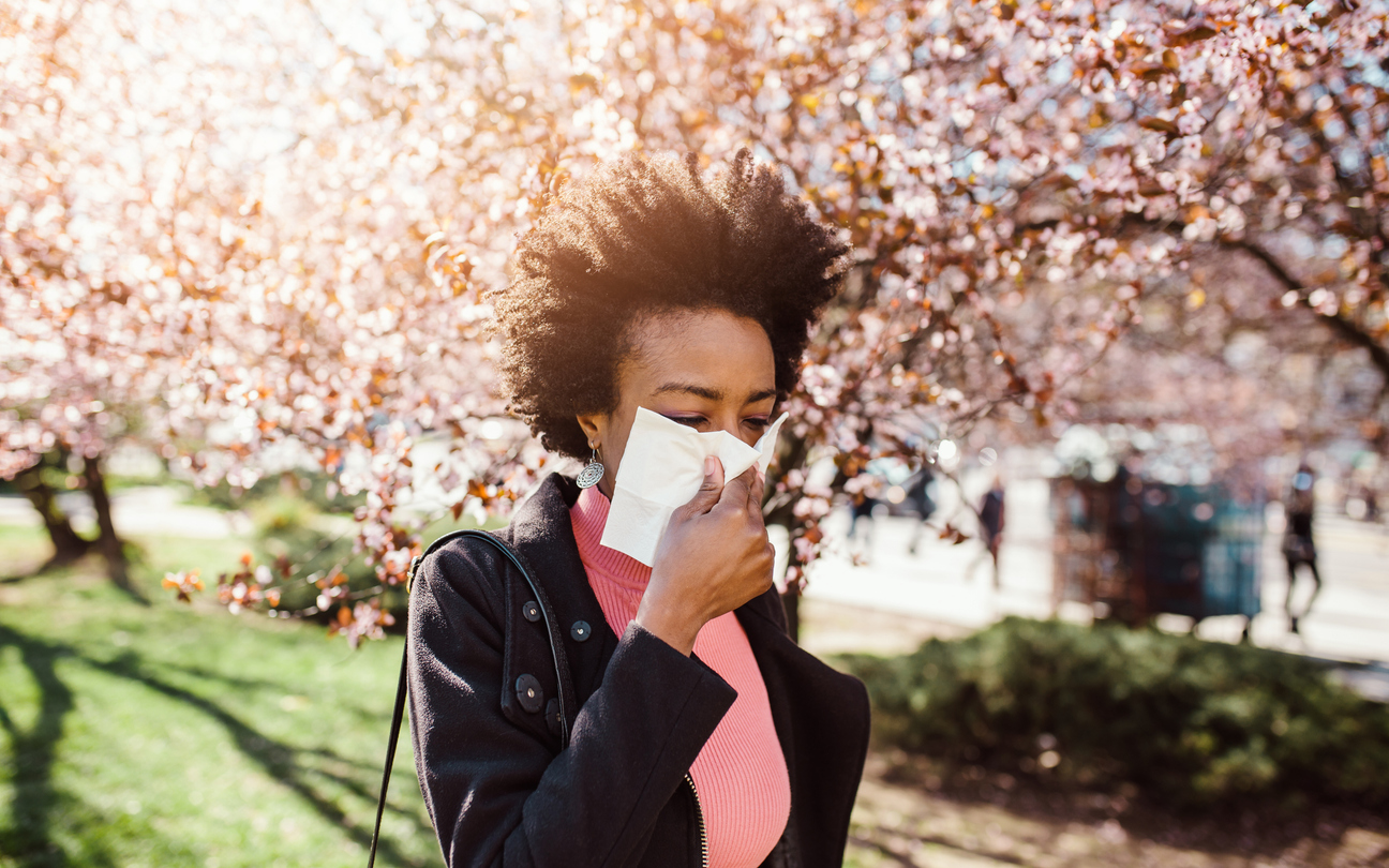 woman-walking-by-blooming-tree-with-tissue-to-address-allergies