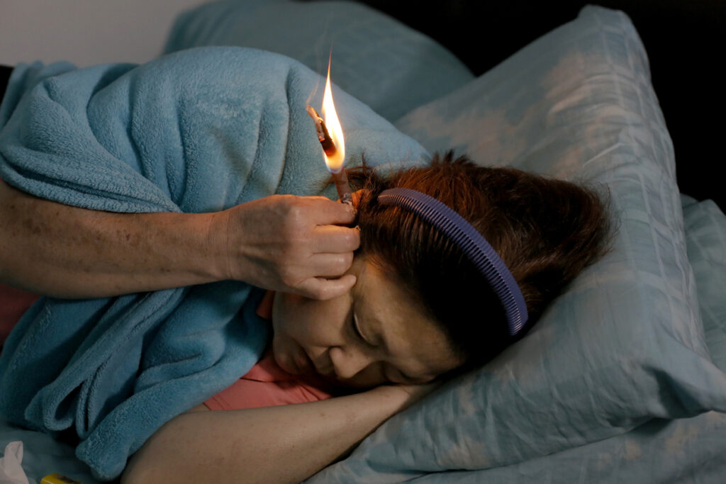 woman-laying-in-bed-ear-candling-to-remove-earwax